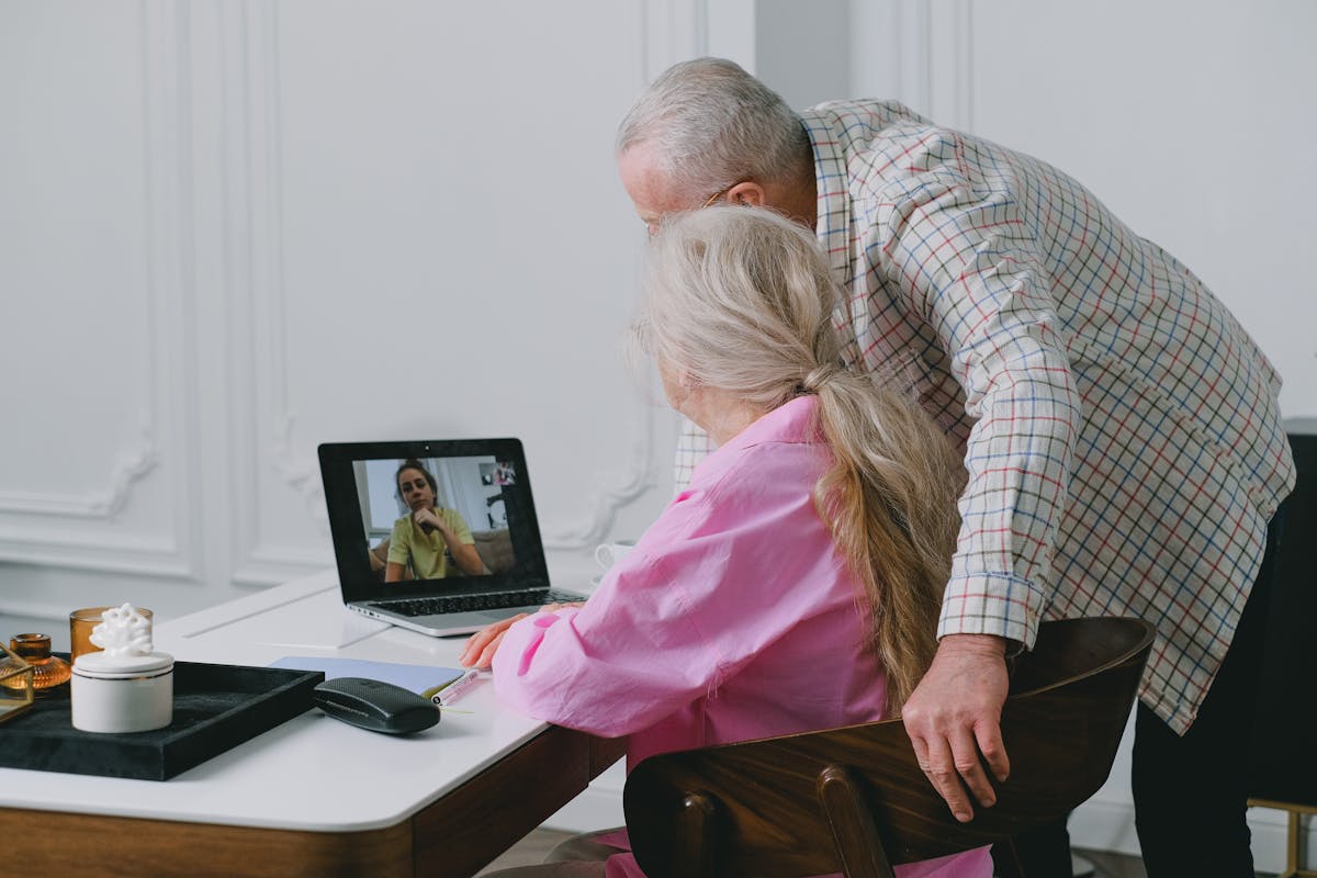 An older couple smiling while video calling family on a laptop